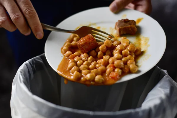 Closeup of a young caucasian man throwing the leftover of a plate of chickpea stew to the trash bin