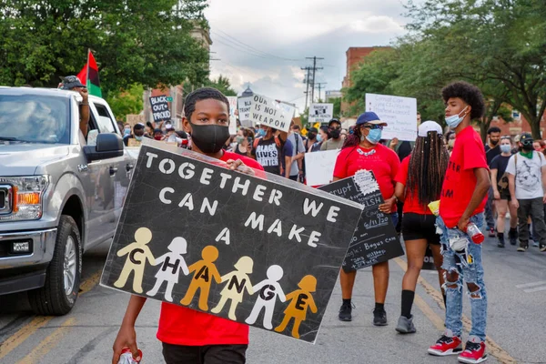 Young boy stands at front of peaceful protest march holding up a sign